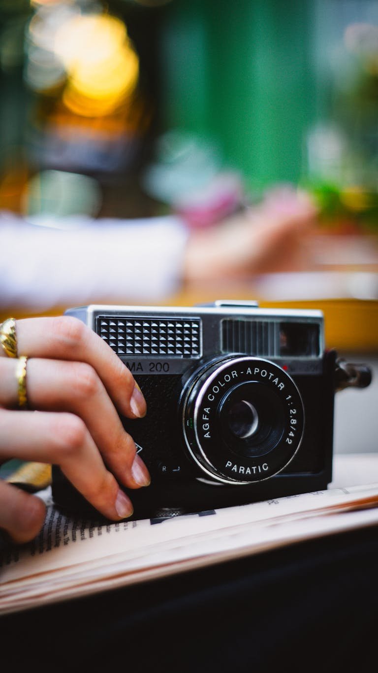 Close-up of a vintage film camera held by a person with blurred urban background.